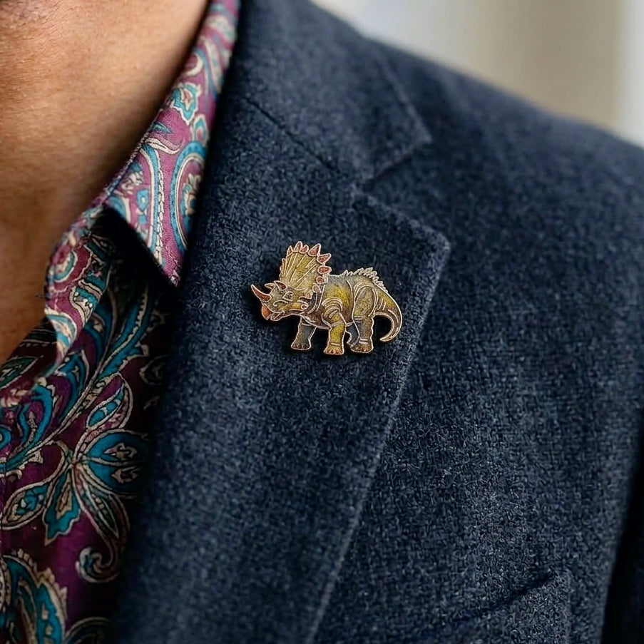A close-up of a man wearing a small Triceratops dino pin on a dark blazer over a paisley shirt.