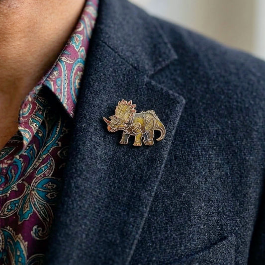 A close-up of a man wearing a small Triceratops dino pin on a dark blazer over a paisley shirt.
