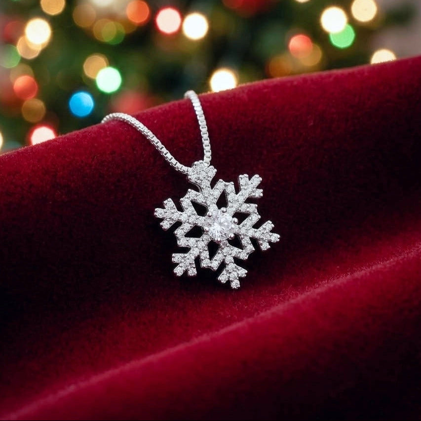 Silver snowflake pendant with bright cubic zirconia crystals on a venetian box chain, resting on dark red velvet material with colourful blurred festive lights in the background.
