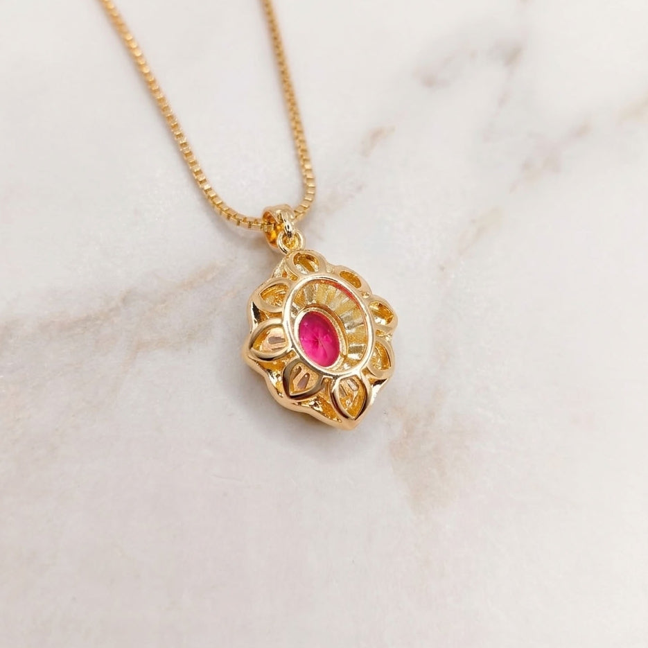 The back of a gold pendant necklace featuring an open metal in the shape of flower petals to let light on the back of the stones. It is hanging from a delicate gold chain on a light marble surface.