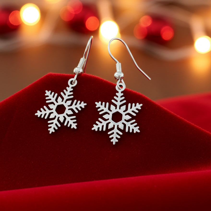 Silver snowflake earrings on a red surface with blurred lights in the background