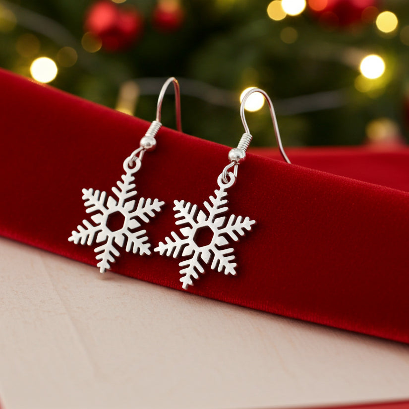 Silver snowflake earrings on a red surface with a blurred Christmas tree in the background
