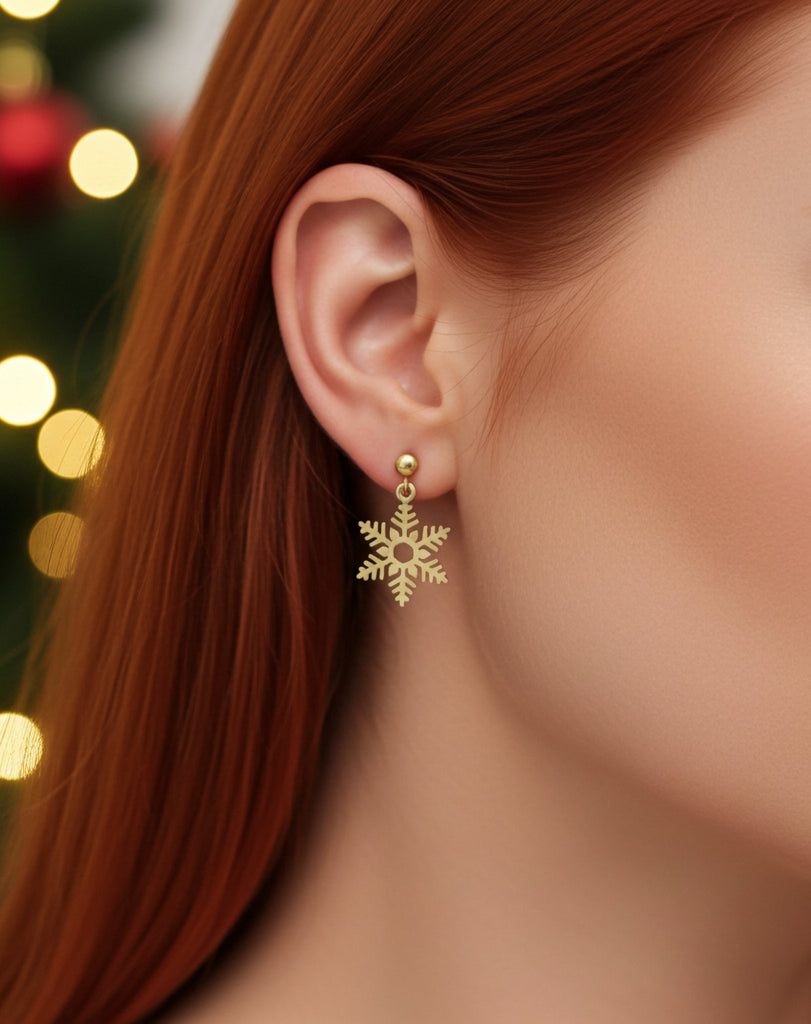Gold snowflake clip on earring worn by a person with a blurred Christmas tree in the background