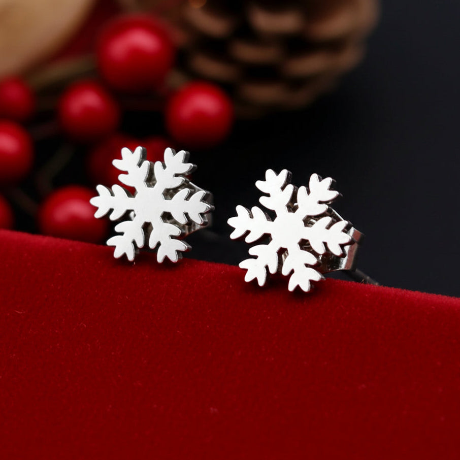 Snowflake stud earrings on a red surface with blurred berries and pine cones in the background