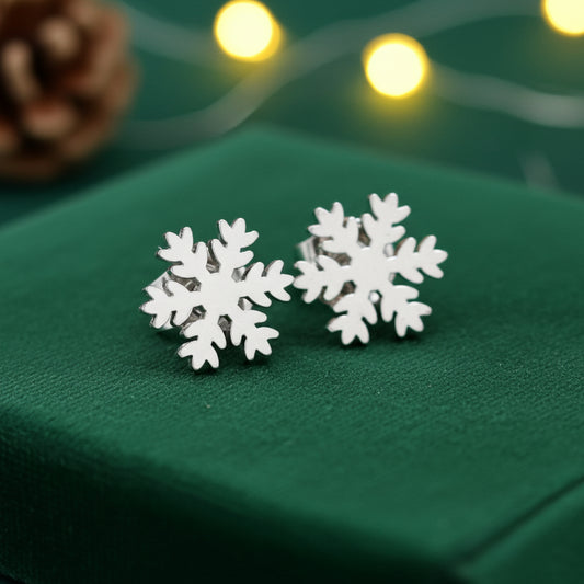 Silver snowflake stud earrings on a green surface with blurred lights in the background