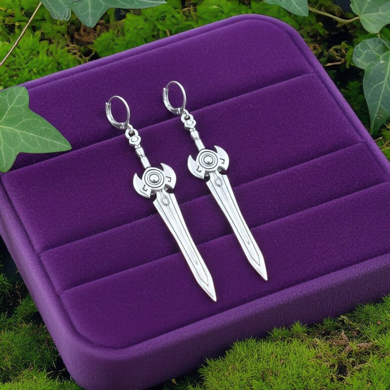 Silver sword earrings on a purple jewelry display with green leaves in the background