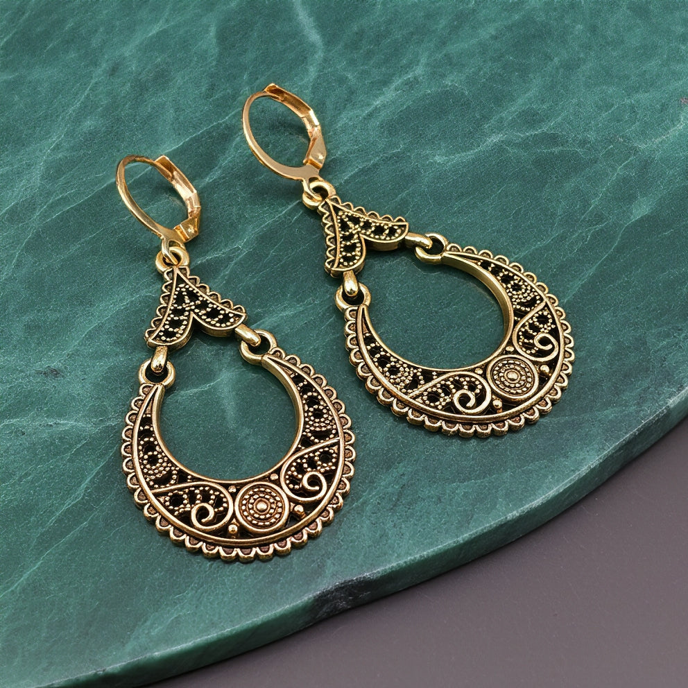 Gold hoop earrings with intricate designs on a green stone surface