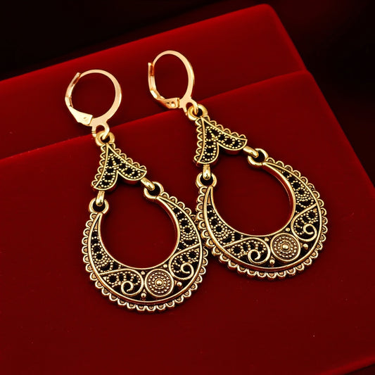 Gold hoop earrings with intricate designs on a red background