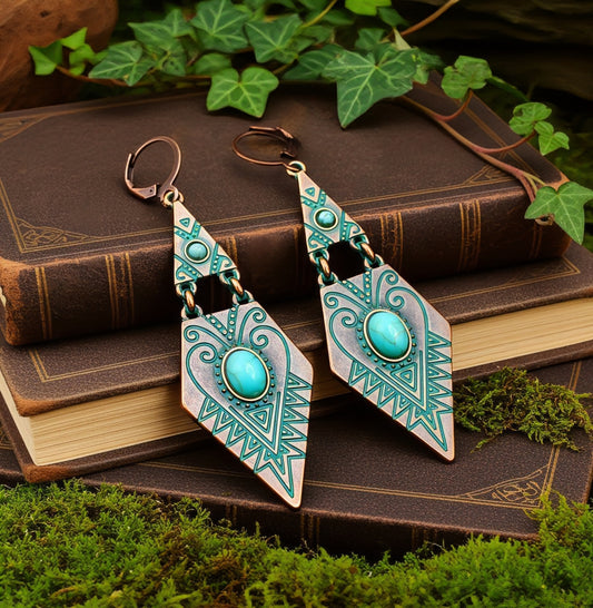 Pair of copper and turquoise ethnic tribal earrings on an old book with green leaves in the background