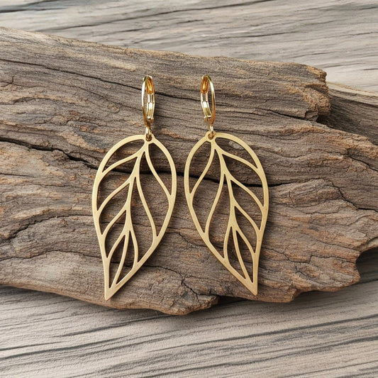 Large gold stainless steel leaf earrings with hoops on a wood background
