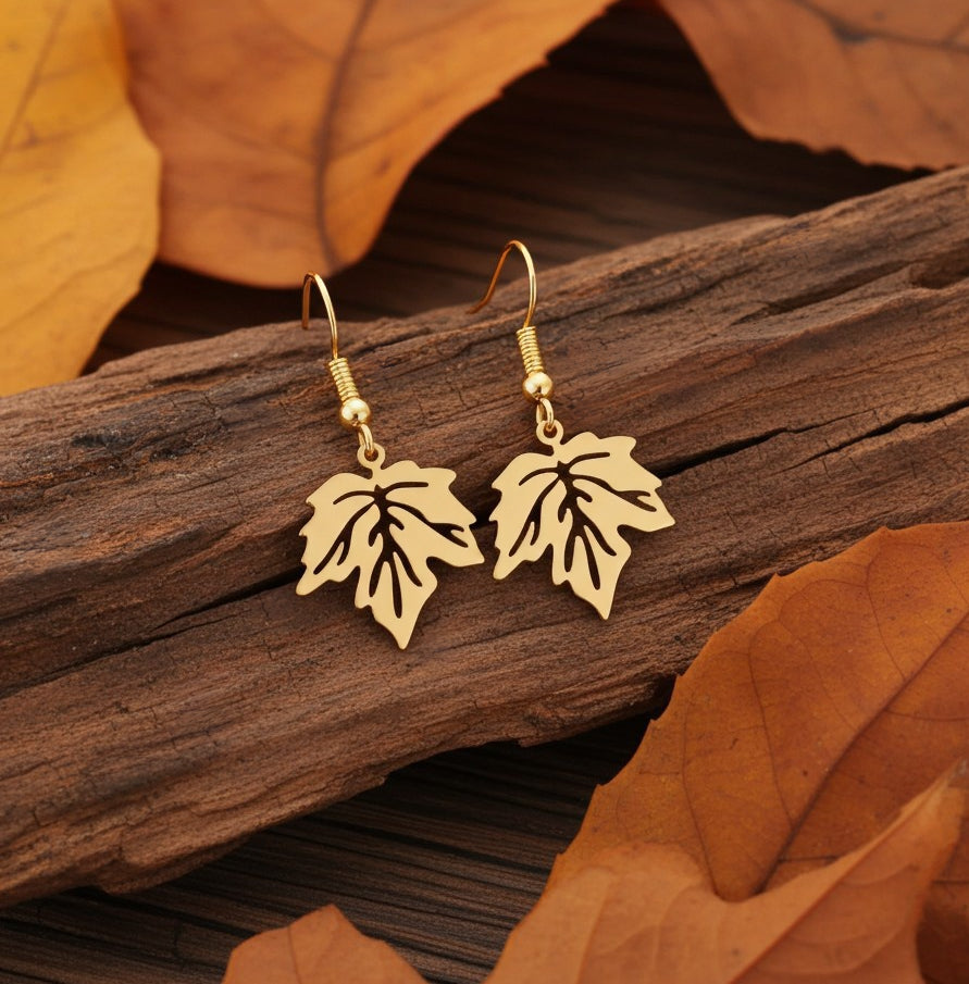 Gold stainless steel leaf earrings with hooks on a wood background with autumn leaves