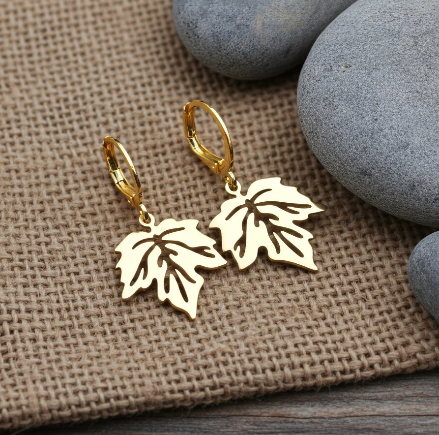 Gold stainless steel leaf earrings with hoops on a rustic background