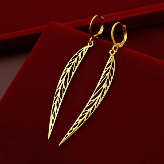 Long pointy gold stainless steel leaf earrings with hoops on a red background