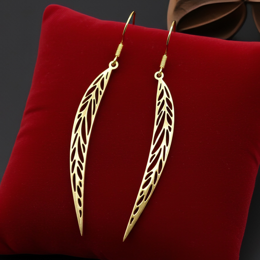 Long pointy gold stainless steel leaf earrings with hooks on a red background
