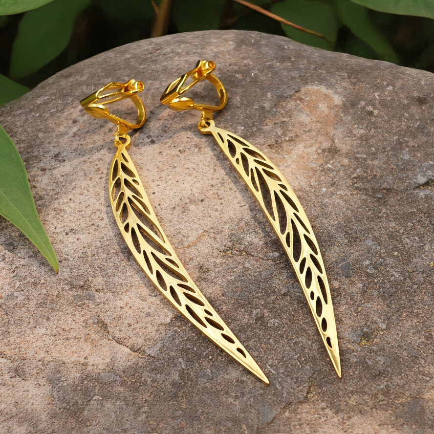 Long gold stainless steel leaf earrings with clip ons on a stone background