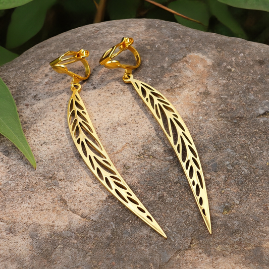 Long gold stainless steel leaf earrings with clip ons on a stone background