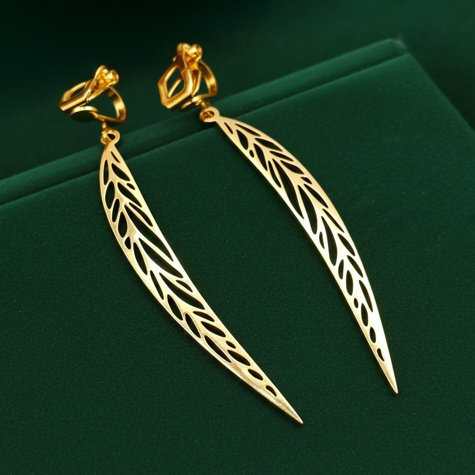 Long pointy gold stainless steel leaf earrings with clip ons on a green background