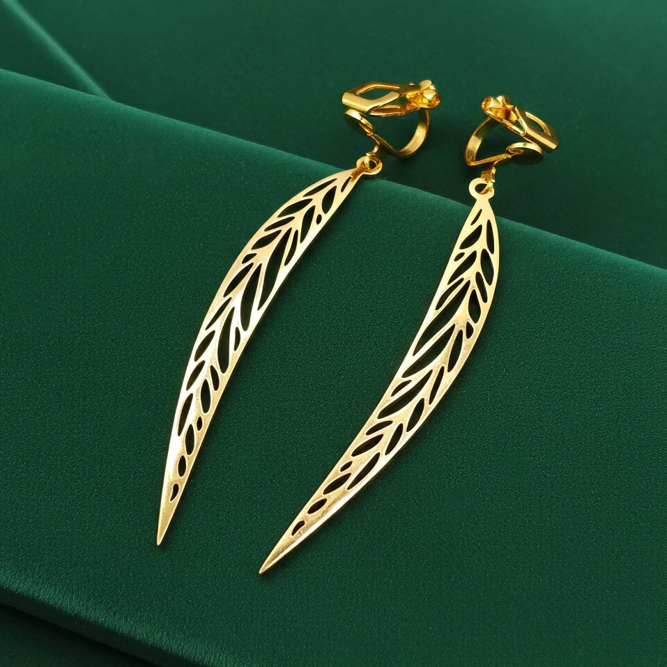 Long pointy gold stainless steel leaf earrings with clip ons on a green background