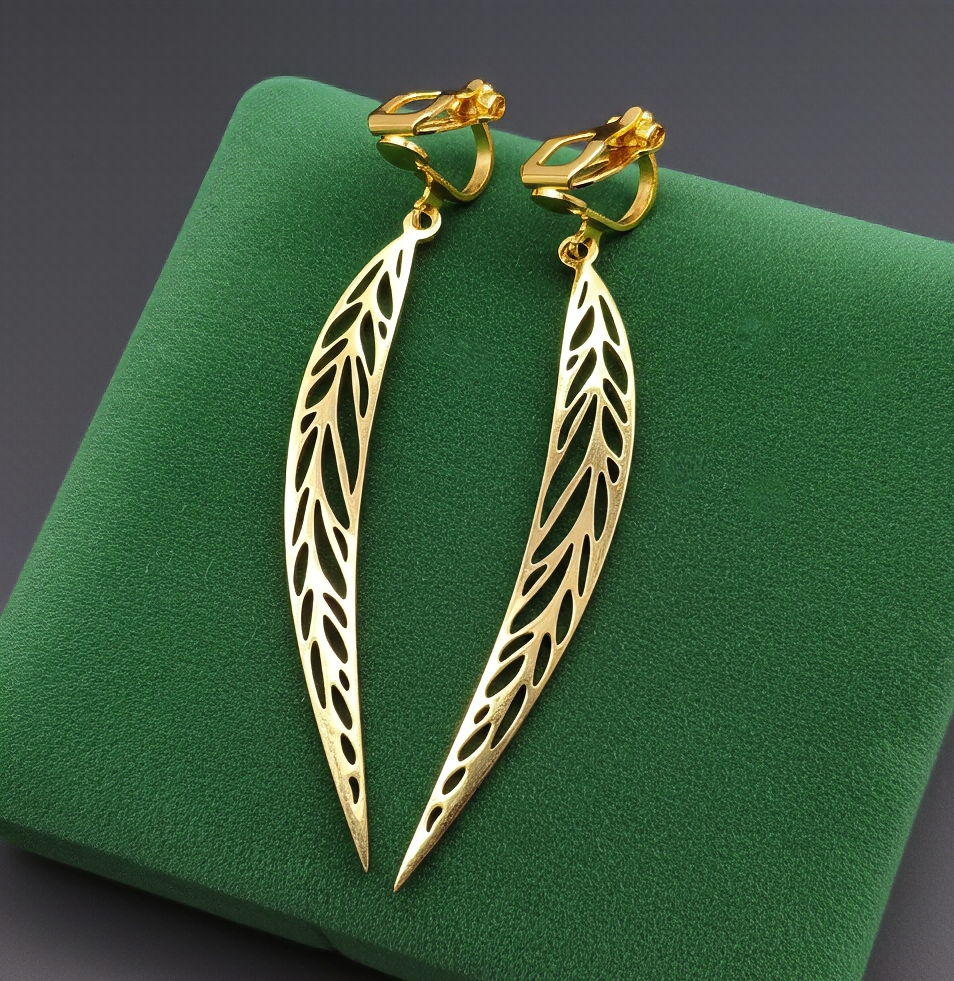 Long gold stainless steel leaf earrings with clip ons on a green background