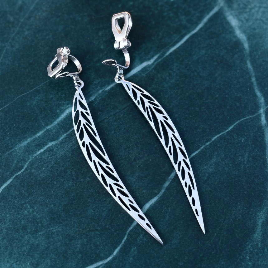 Long pointy stainless steel leaf earrings with silver clip-ons on a teal marble background 