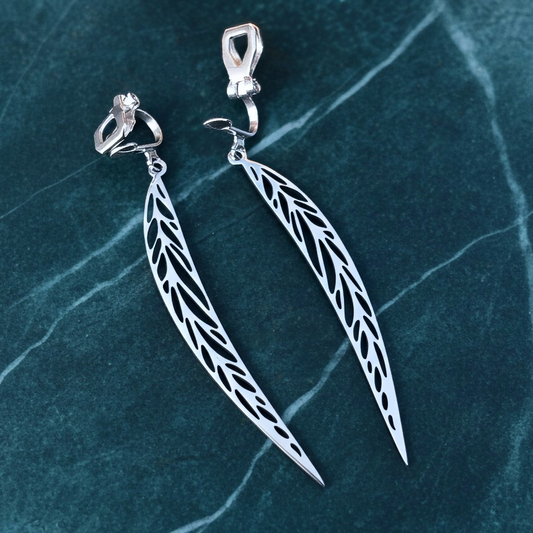 Long pointy stainless steel leaf earrings with silver clip-ons on a teal marble background 