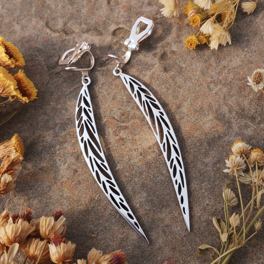 Long pointy stainless steel leaf earrings with silver clip-ons on a stone background with dried flowers