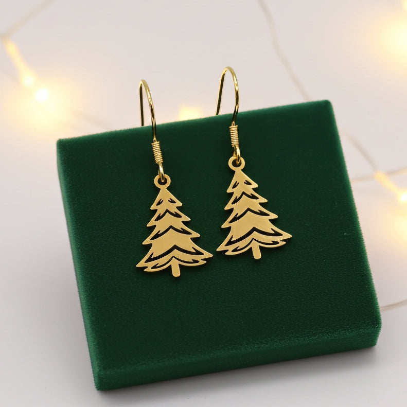 Festive Christmas tree earrings made out of gold stainless steel and hook earrings, on green velvet with lights in the background.