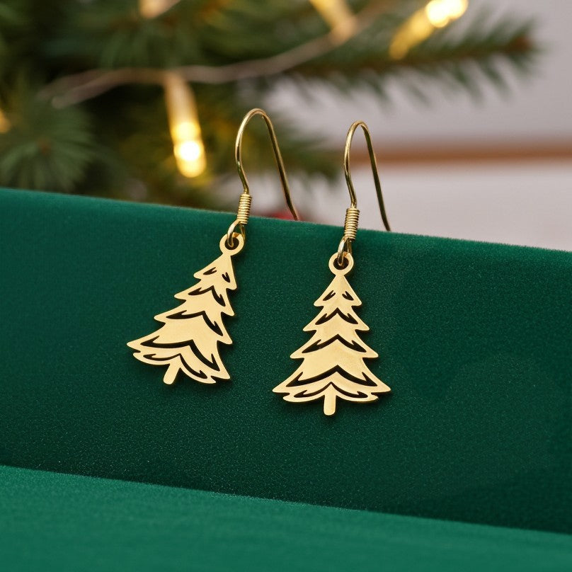 Festive Christmas tree earrings made out of gold stainless steel and hook earrings, on green velvet with lights in the background.