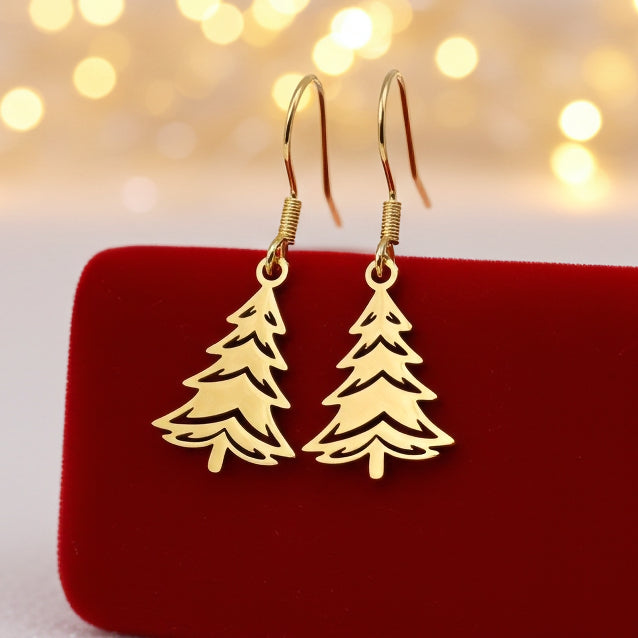 Festive Christmas tree earrings made out of gold stainless steel and hook earrings, on red velvet with lights in the background.