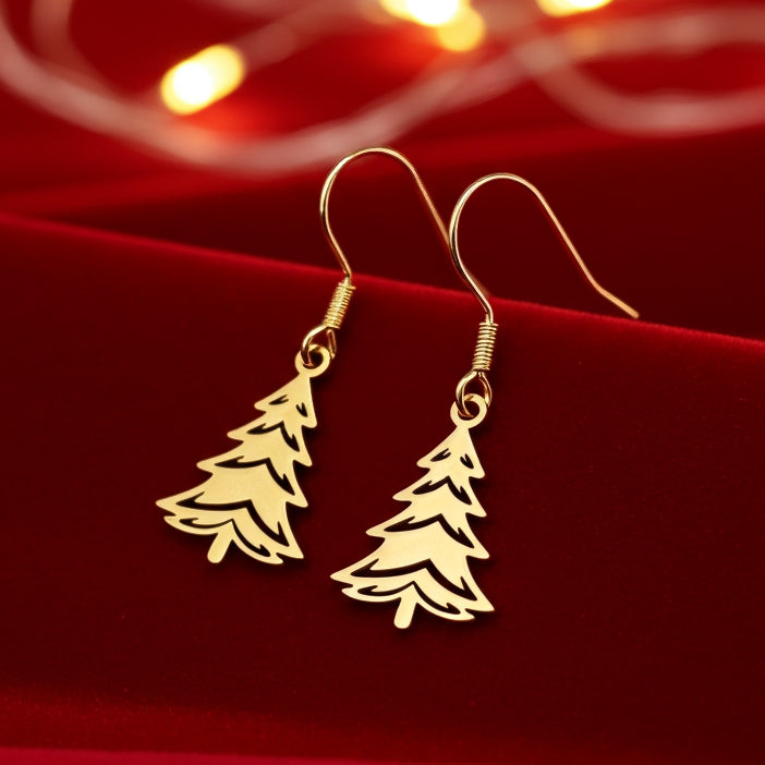 Festive Christmas tree earrings made out of gold stainless steel and hook earrings, on red velvet with lights in the background.
