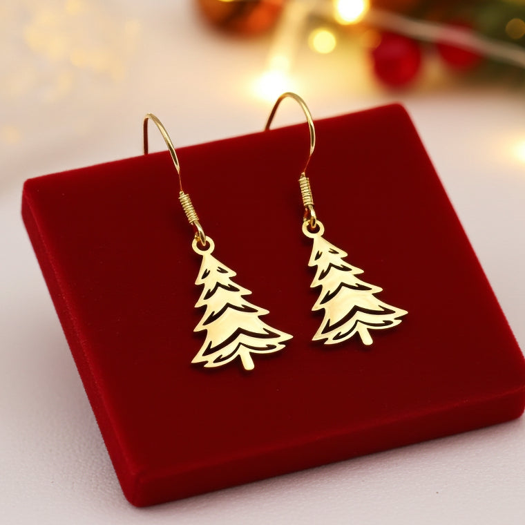 Festive Christmas tree earrings made out of gold stainless steel and hook earrings, on red velvet with lights in the background.