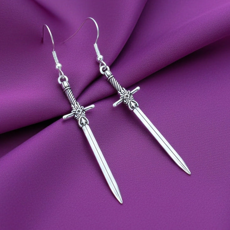 Fantasy style silver sword earrings on a purple fabric background