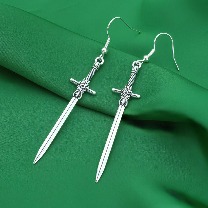 Fantasy style silver sword earrings on a green fabric background