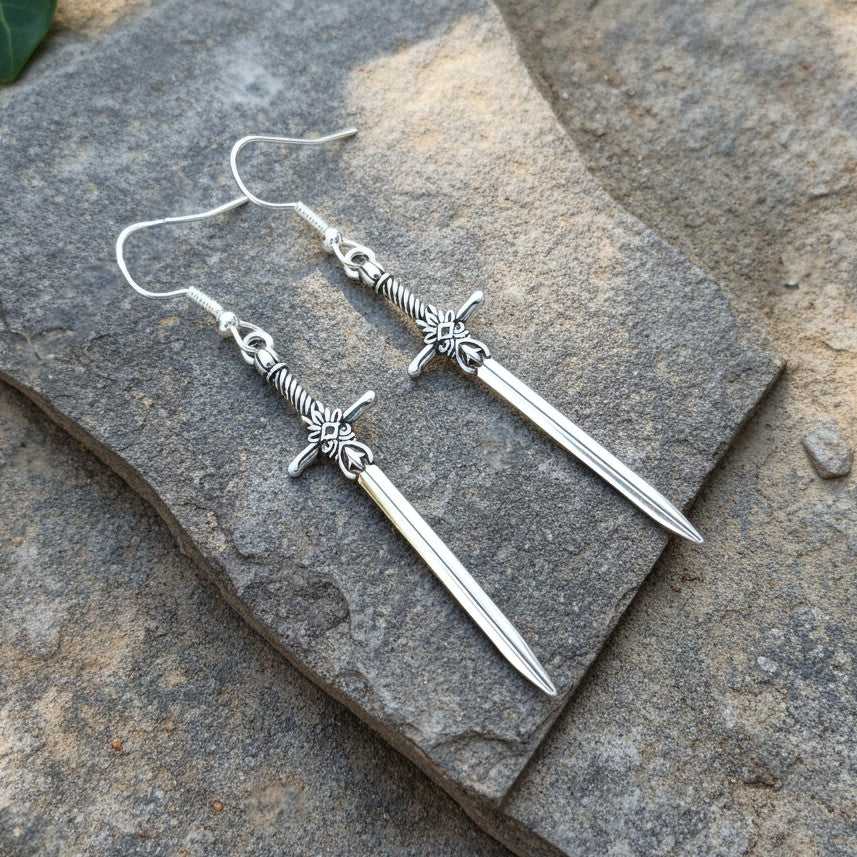 Silver sword earrings on a stone surface