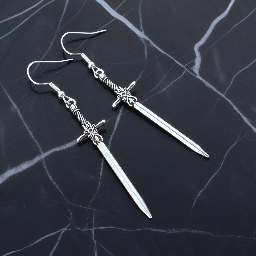 Silver sword-shaped earrings on a dark marble surface