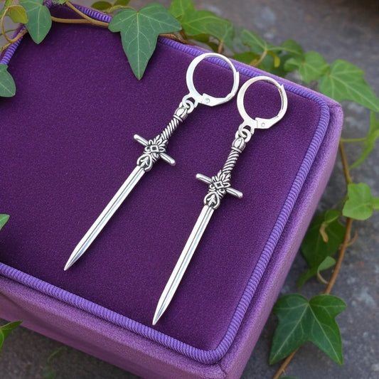 Fantasy style silver sword earrings with hoops on a purple velvet box and ivy in the background
