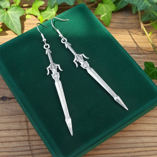Fantasy style silver sword earrings on a green velvet background with light coming in