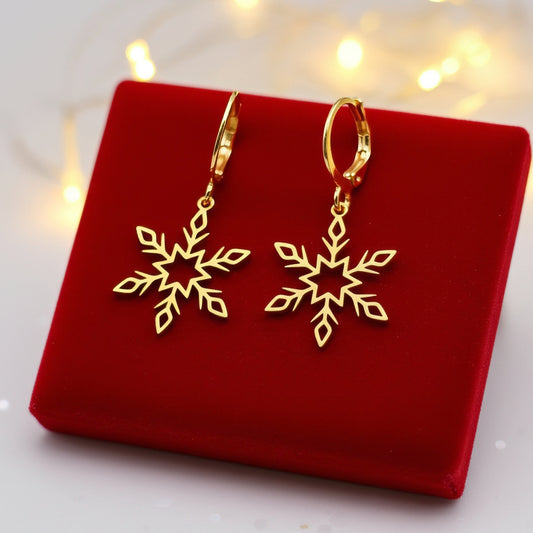 Dainty gold snowflake earrings with hoops on a red fabric background with festive lights behind