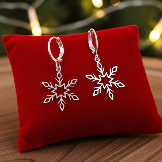 Dainty silver snowflake earrings with hoops on a red fabric background with festive lights behind