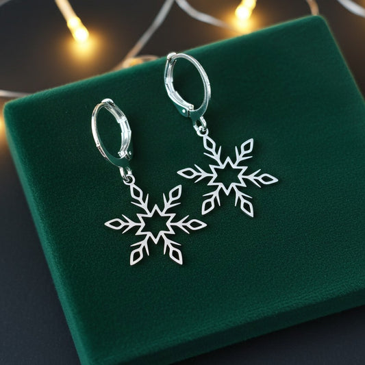 Dainty silver snowflake earrings with hoops on a green fabric background with festive lights behind