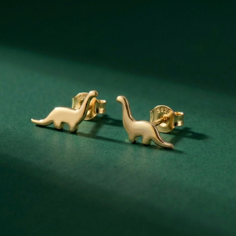 Gold dinosaur-shaped earrings with S925 on them, on a green background
