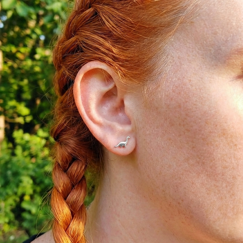 Person with braided red hair wearing a small dinosaur earring outdoors.