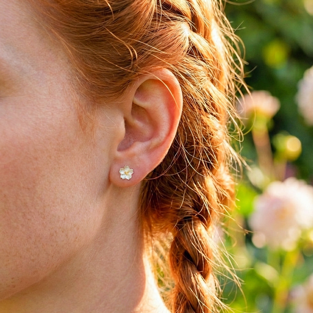 Close-up of a person's ear with a flower-shaped earring, blurred floral background