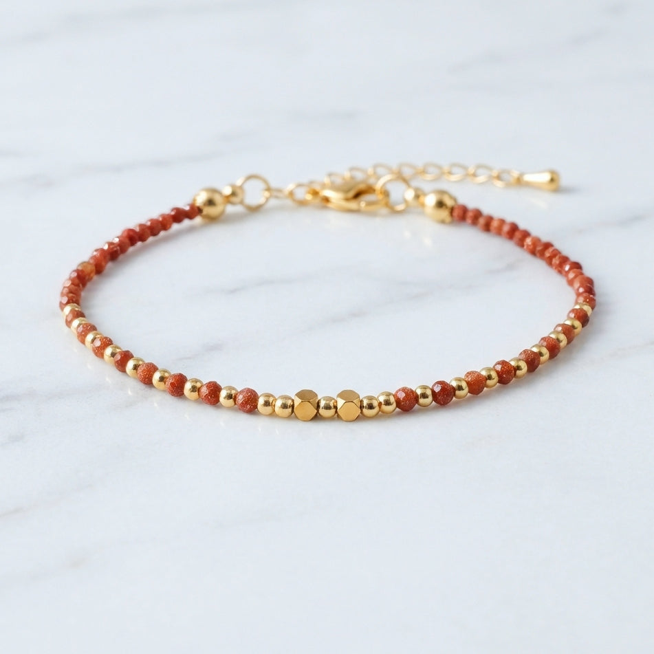 A dainty bead bracelet with sparkly gold sandstone gemstone beads on a marble background