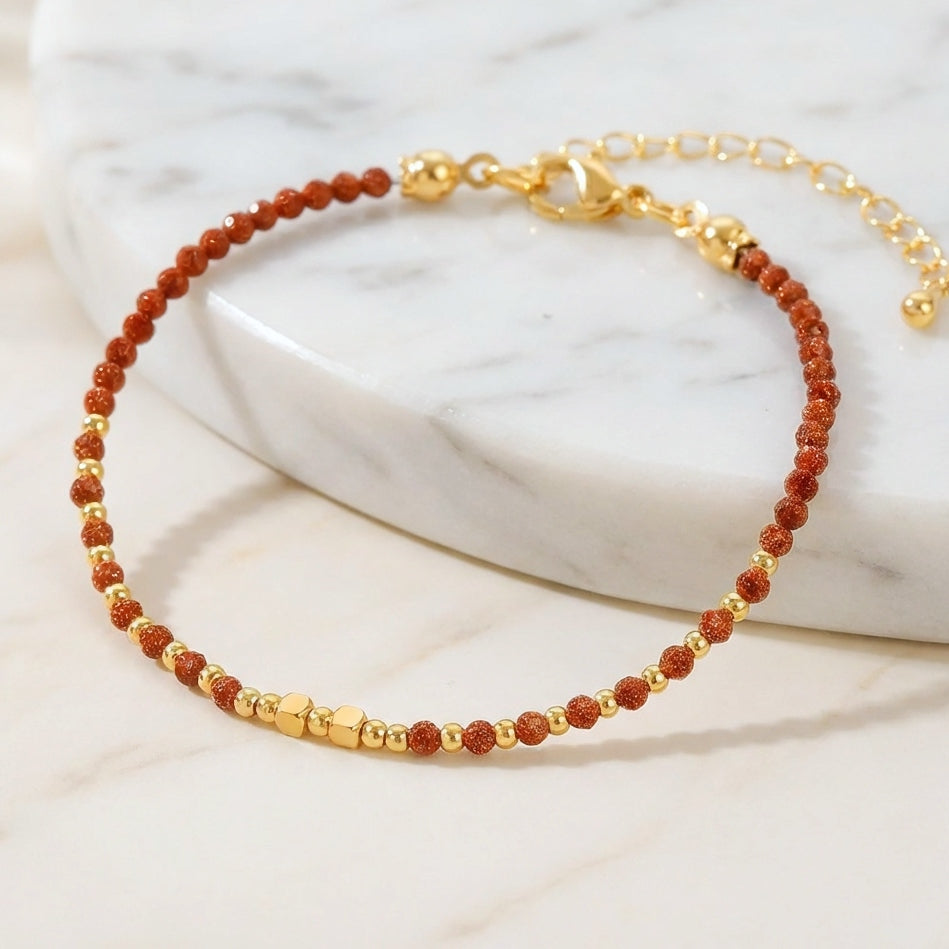 A dainty bead bracelet with sparkly gold sandstone gemstone beads on a marble background