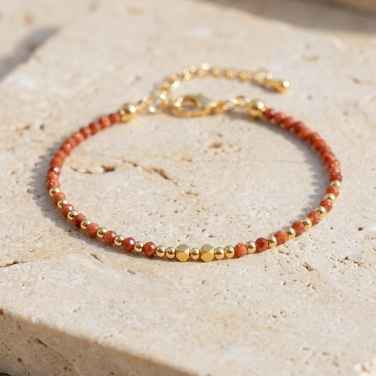 A dainty bead bracelet with sparkly gold sandstone gemstone beads on a light stone background