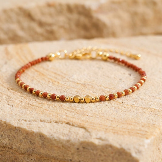 A dainty bead bracelet with sparkly orange gold sandstone gemstone beads on a light stone background