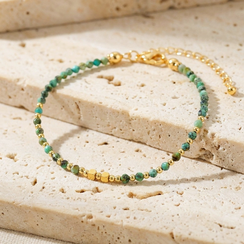 Natural turquoise gemstone beaded bracelet with gold clasp, on a stone background