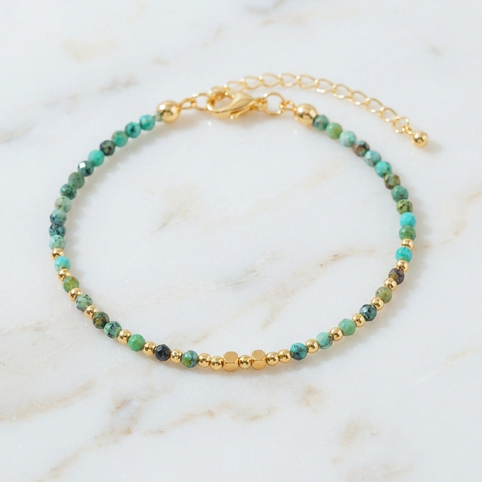 Natural turquoise gemstone beaded bracelet with gold clasp, on a marble background