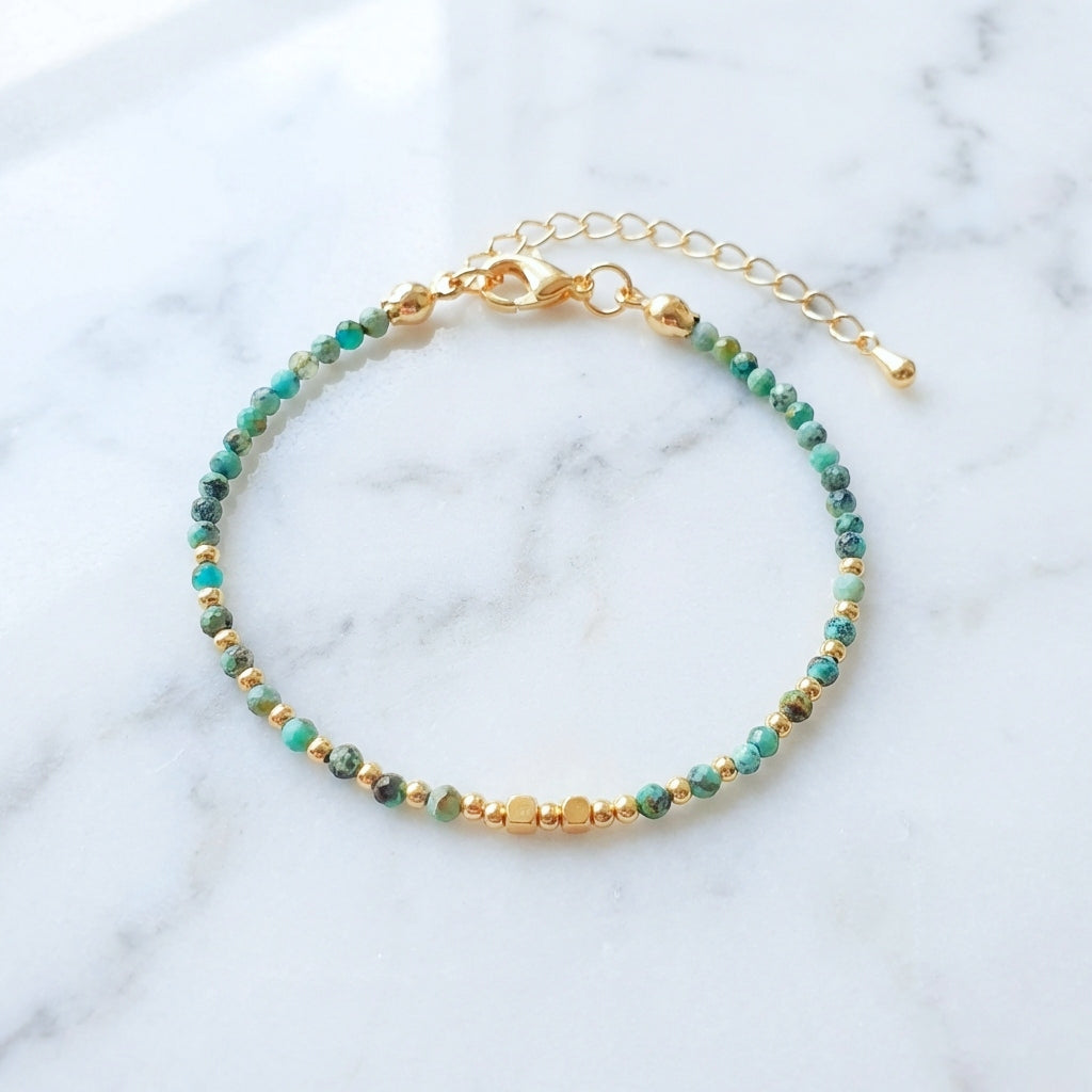 Natural turquoise gemstone beaded bracelet with gold clasp, on a marble background